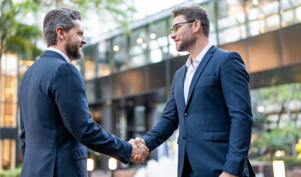 Handshake with business partner in the city for greeting. Handshake between two business men. Two businessmen shaking hands on city street. Business men in suit shaking hands outdoors. Business team.
