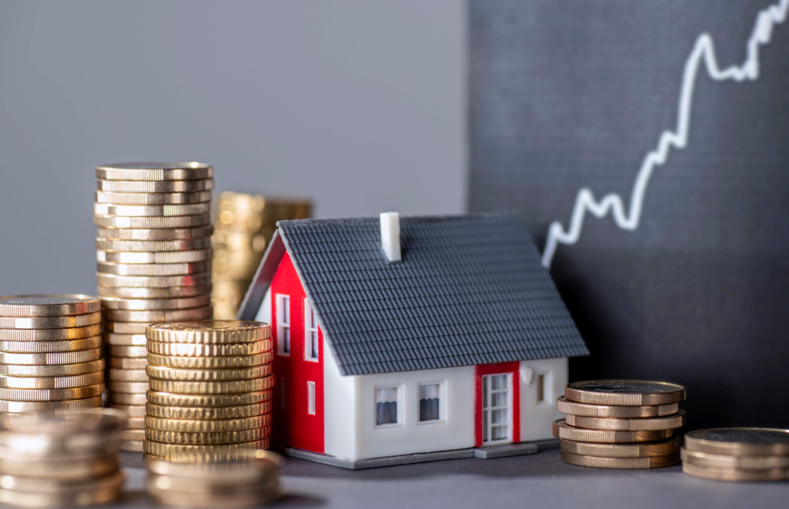 Haus mit Geldstapeln und einer steigenden Kurve, die steigende Immobilienpreise symbolisiert